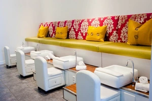 Modern nail salon with white pedicure chairs, green bench seating, red floral cushions, and yellow pillows.