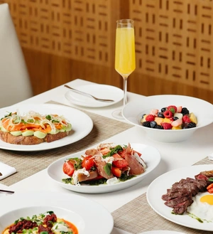 A table set with assorted brunch dishes, fresh fruit, and a glass of orange mimosa.