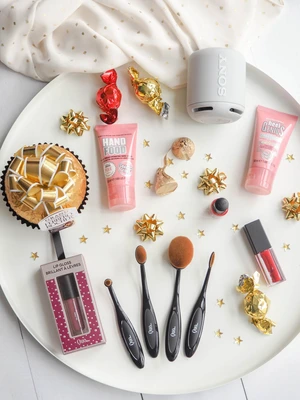 Round tray with makeup brushes, hand creams, lipstick, candies, cupcake, and a small gray SONY speaker.