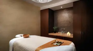 A tranquil spa room with a massage table, soft lighting, towels, and candles on a wooden counter.