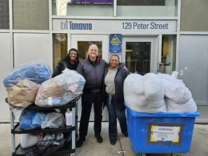 Three people stand smiling outside a Toronto building with carts of bagged donations in front of them.