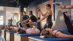 Trainers assist people lying on tables with leg stretches in a fitness or physical therapy studio.