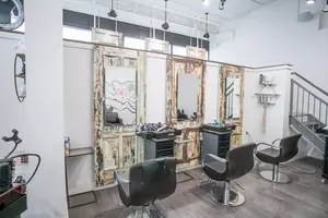 Modern hair salon with three black styling chairs and distressed wooden mirrors against a white wall.