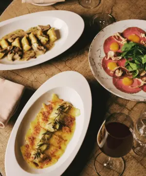 Three plates of gourmet Italian dishes and a glass of red wine on a rustic table.