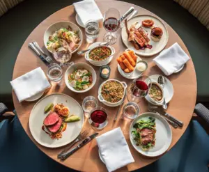 A round table set with plates of gourmet food, wine glasses, and white napkins, seen from above.