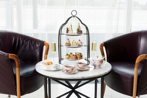 Afternoon tea set with pastries, tea cups, and champagne on a table between two armchairs.