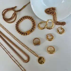 Assorted gold jewelry including necklaces, bracelets, rings, and hoop earrings displayed on a white surface.