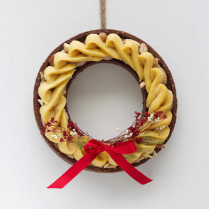 A round cake decorated like a wreath with yellow frosting, small flowers, and a red ribbon on white background.