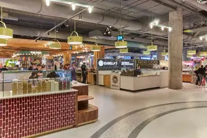 Indoor food court with various vendor stalls, bright lighting, and people ordering food.