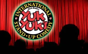 Yuk Yuk's International Stand-Up Comedy logo in front of red curtains with audience silhouettes.